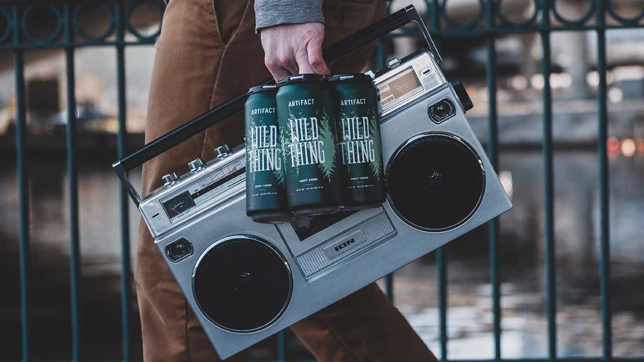 Guy carrying holding a 4-pack of Wild Thing cider and a boombox