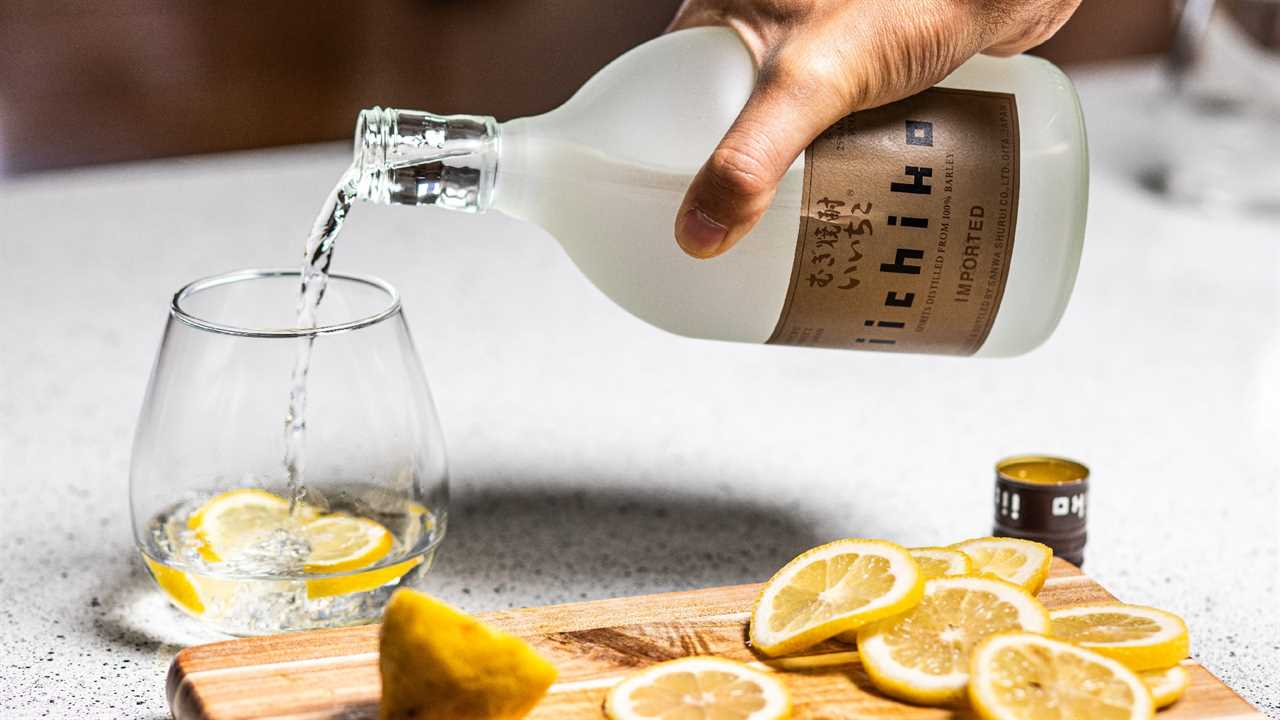 Man pouring bottle of clear spirit into glass next to cutting board of lemon slices