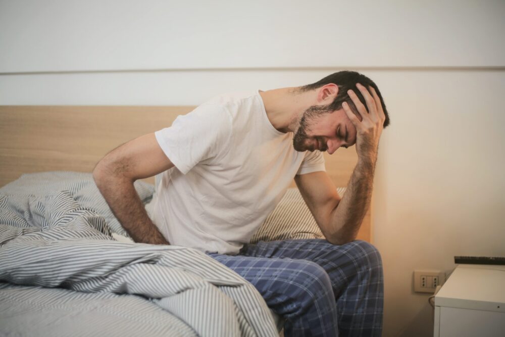 man waking up holding head and stomach because of inflammation