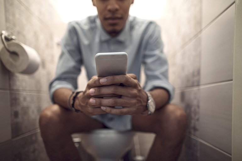 Man on toilet searching on his phone about what different types of poop mean
