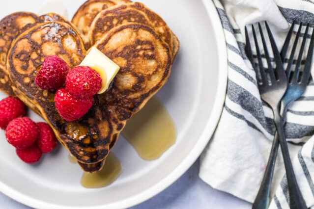 Heart-shaped pancakes topped with raspberries, butter, and syrup, two forks