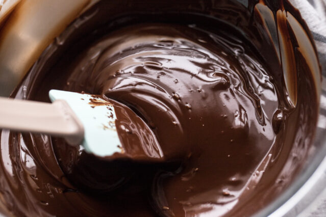 Melted chocolate in a bowl being stirred with a spatula.