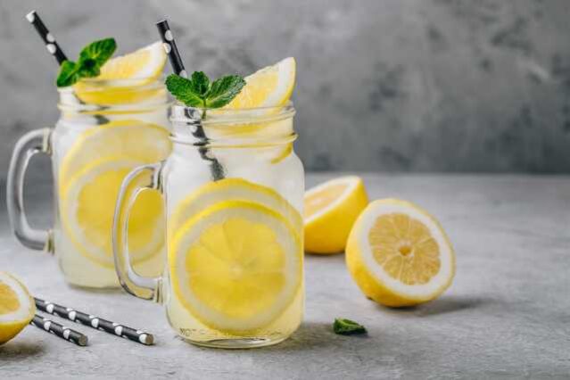 Two jars of water with lemon slices and straws against a gray background