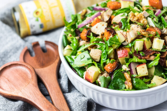 Bowl of salad with spinach, bacon, & cubed apples & butternut squash; wooden salad server, Primal Kitchen Honey Mustard Dressing