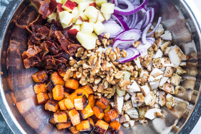 Chicken, bacon, butternut squash, walnuts, and red onion in a large bowl.