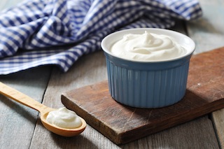 Yogurt in a blue ramekin, blue checkered napkin, spoon with yogurt on the table next to the ramekin