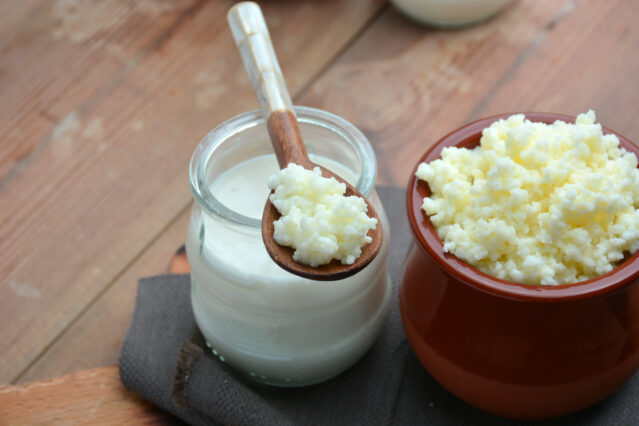 Kefir in a jar, kefir grains in a bowl and in a spoon balance atop the jar