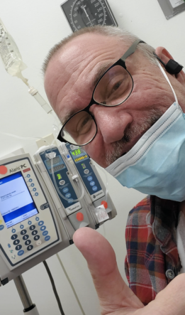 Man in surgical mask with chemotherapy equipment gives a thumbs up to camera