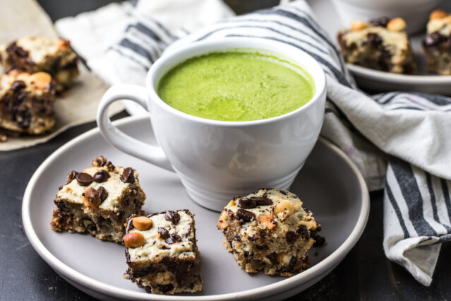 Three macadamia cookie bars on a plate with a mug of Primal Kitchen Matcha Collagen Latte