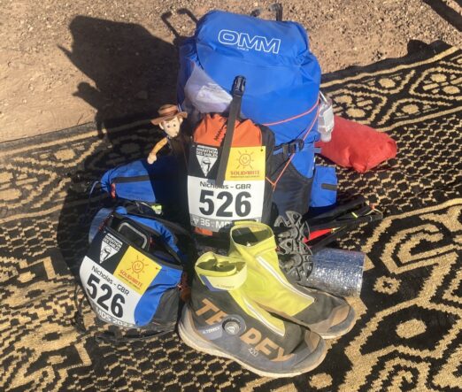 Running gear bag with shoes and backpack sitting on a black and beige pattered carpet