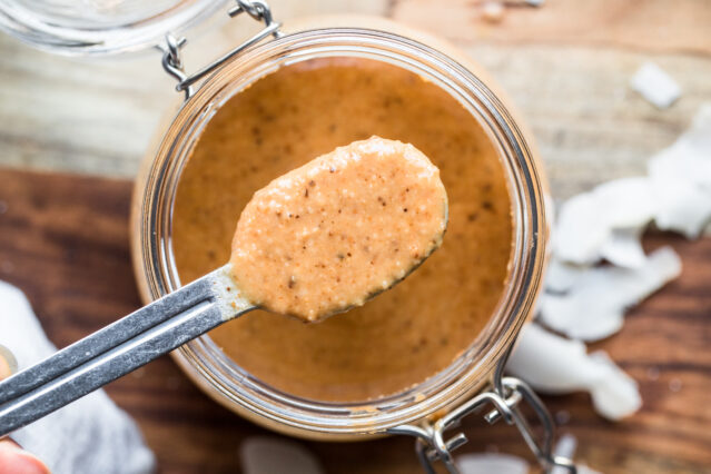 Overhead shot of a jar of homemade coconut butter with a hand spooning out a spoonful.