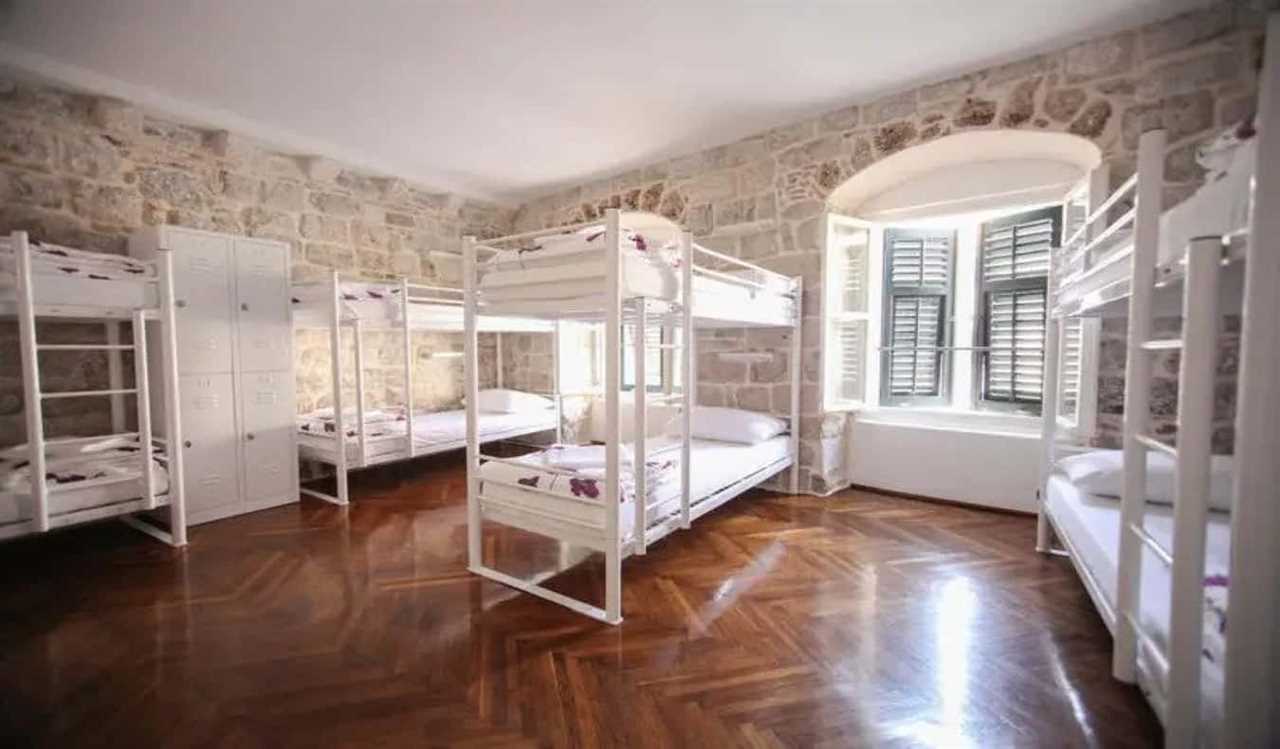 Dorm room with bunk beds, wood floors, and stone walls at Hostel Angelina in Dubrovnik, Croatia.