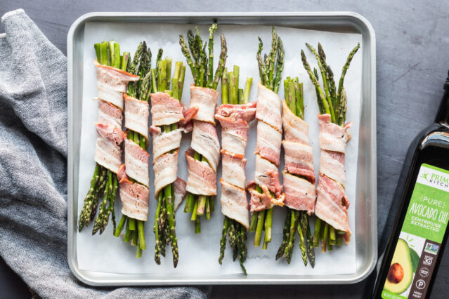 asparagus wrapped in uncooked bacon on a sheet pan
