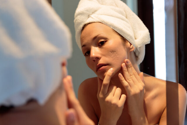 Woman in towel examining her skin in the mirror