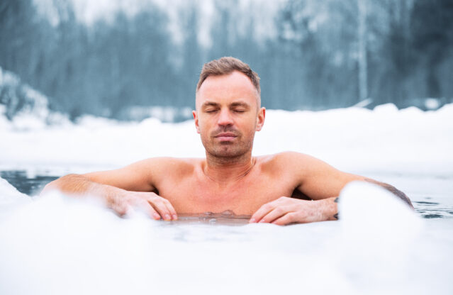 Man submerged in icy lake up to his chest, eyes closed looking peaceful.