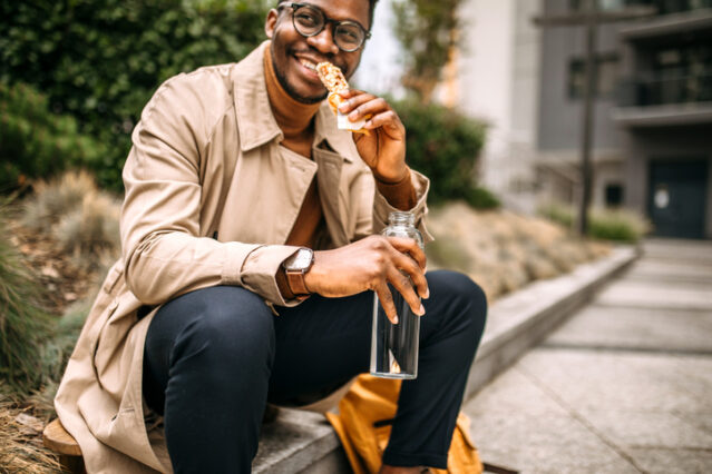 Man eating a granola bar while sitting in front of building