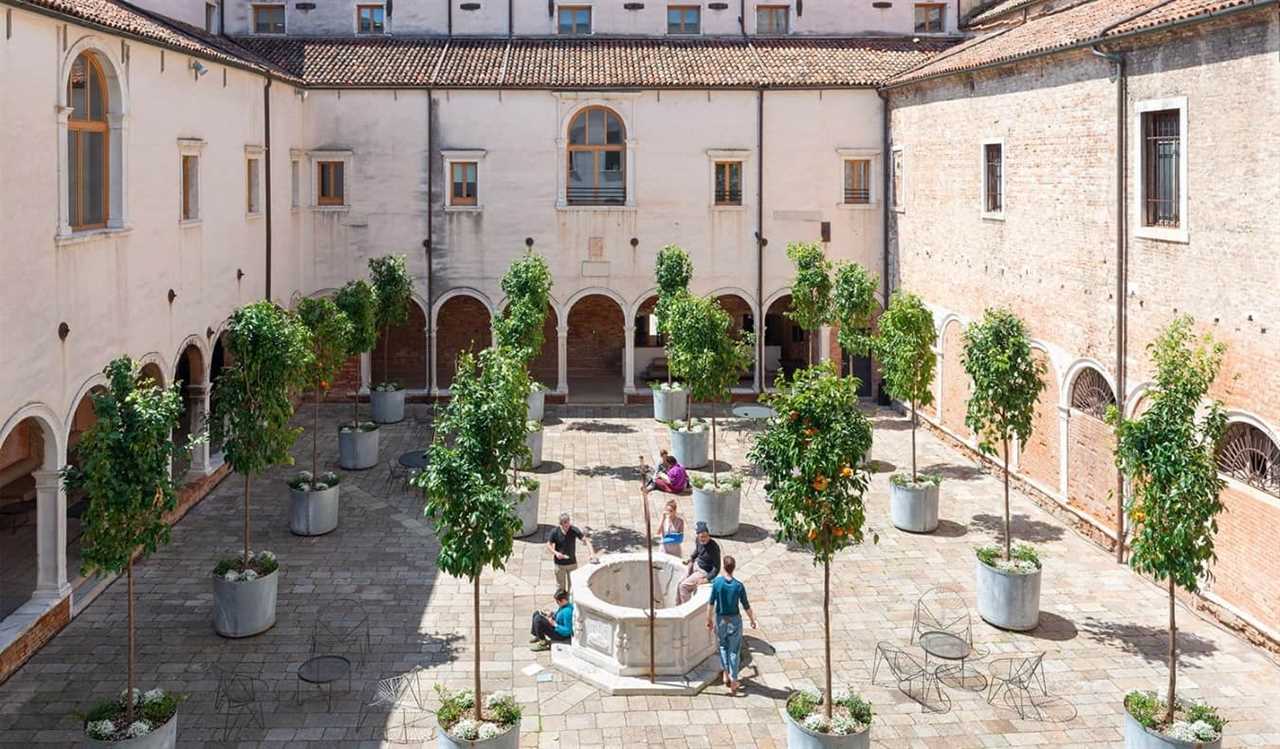 Historic cloister filled with orange trees and people standing around chatting at Combo Venezia, a hostel in Venice, Italy.