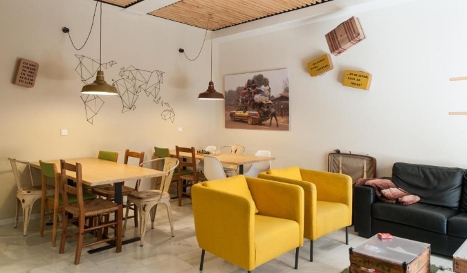 Eclectic common area of The Nomad Hostel with wooden tables and bright yellow lounge chairs in Sevilla, Spain
