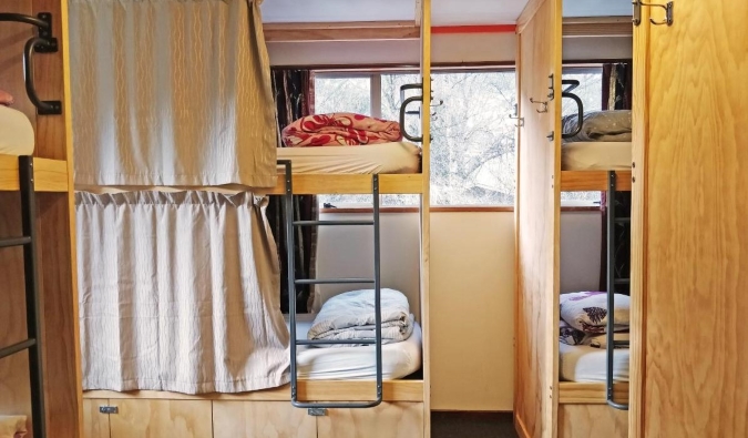 Wooden bunk beds with privacy curtains at The Flaming Kiwi Backpackers hostel in Queenstown, New Zealand