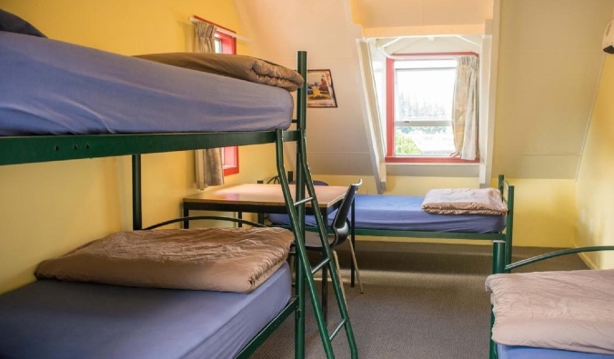 Simple metal bunk beds in a sunny yellow room at Southern Laughter Backpackers hostel in Queenstown, New Zealand