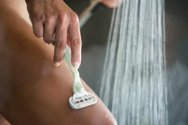 Woman shaving in the shower, which can lead to pimples in the vaginal area including the labia