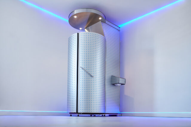 Silver cryotherapy chamber in empty white room.