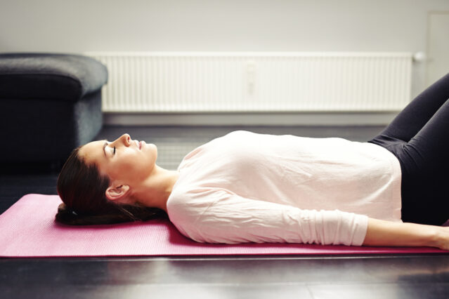 Woman laying on back on pink yoga mat