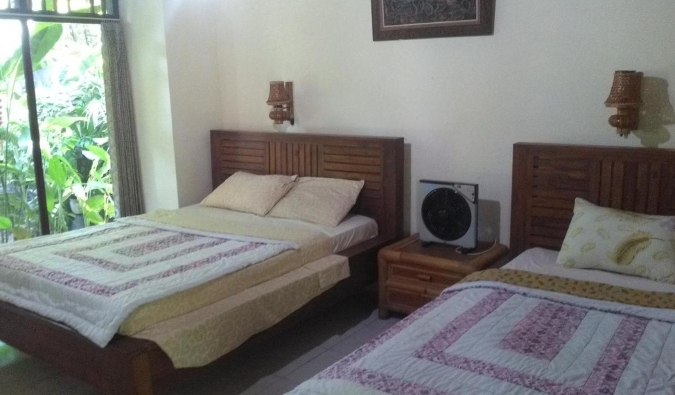 Two double beds with traditional Balinese furnishings at Indraprastha Guest House in Ubud, Bali