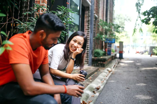 Couple sitting outside on first date, smiling and laughing to appear more attractive