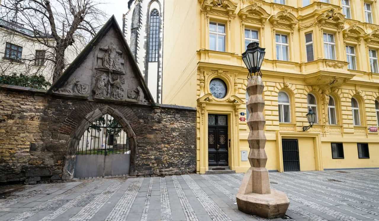 Cubist lamppost in front of a historic yellow building and a gated archway, in Prague, Czech Republic