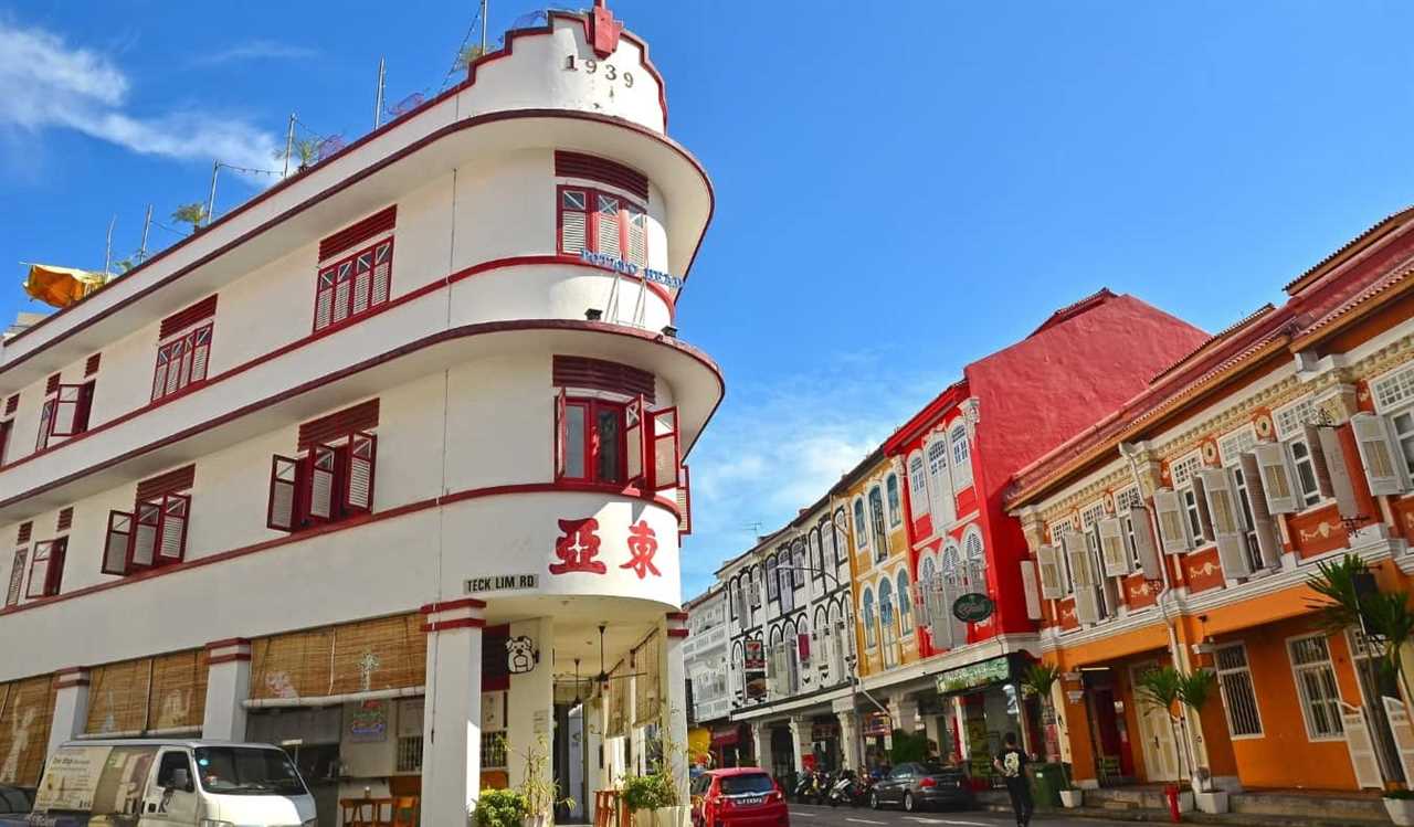 A triangular shaped white building trimmed with red and decorated with Chinese characters, on a street with other colorful buildings in Chinatown, Singapore