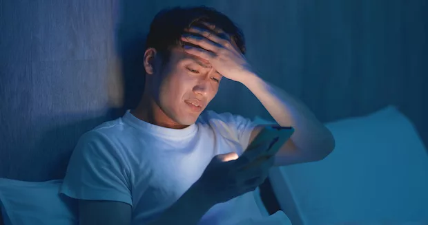 Worried man looking at his phone in the middle of the night, suffering from poor sleep