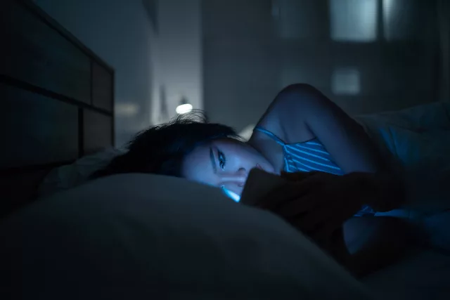 Woman on her phone struggling to sleep in bed due to blue light exposure