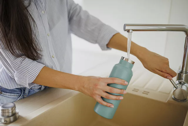 Woman filling up water bottle to hydrate according to the 75 Hard rules