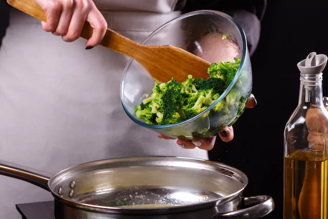 woman cooking broccoli that can lead to bloating at night 