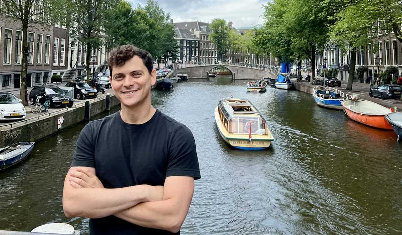 Nomadic Matt posing by a narrow canal in sunny Amsterdam