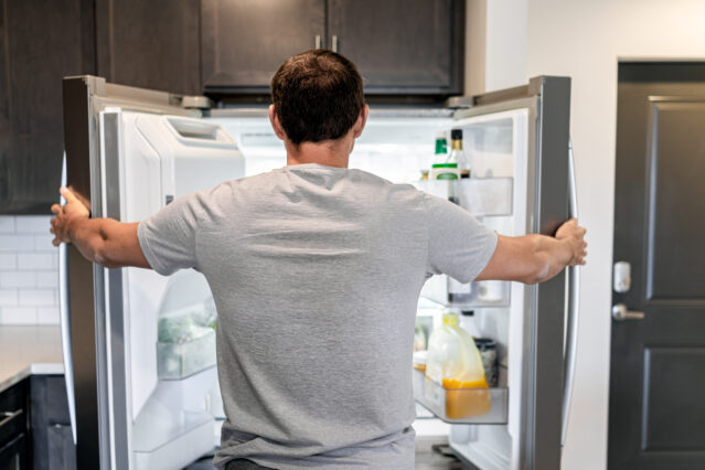 Back of man looking into open fridge deciding what to eat