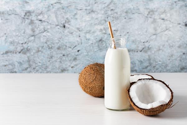 bottle of coconut milk next to coconuts | Coconut Milk Benefits