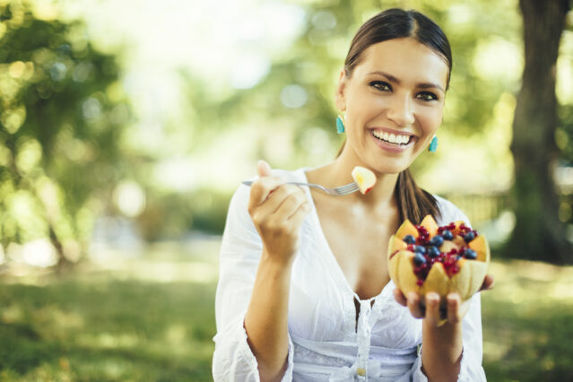 Woman holding a cantaloupe bowl with berries inside smiling into camera.
