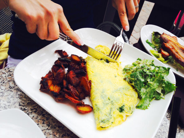 Cropped image of woman having spinach feta omelette served with bacon 