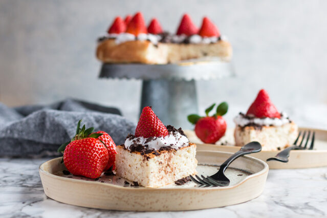 Piece of angel food cake topped with a fresh strawberry, with the remaining cake on a cake stand in the background.