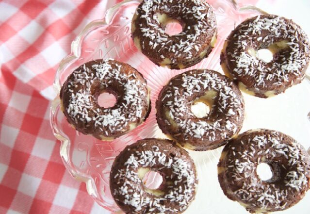 Donuts on crystal platter dusted with shredded coconut, red and white checked tablecloth.