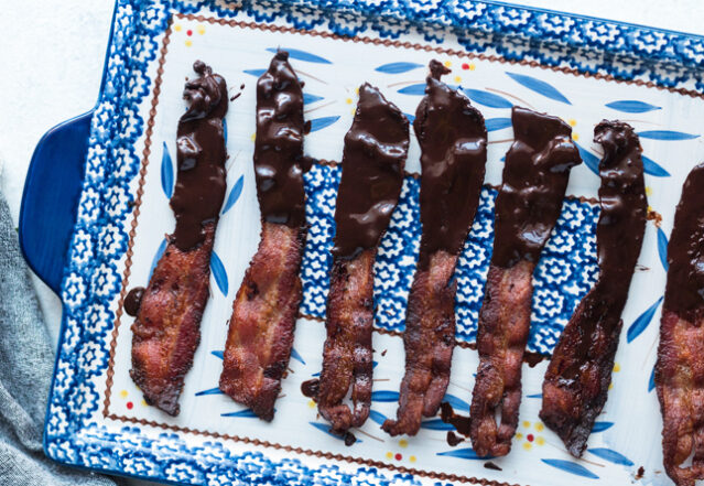 Bacon strips dipped in chocolate on a blue and white tray.