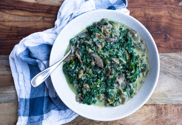 Creamed spinach in white bowl with spoon on wooden background, blue checked napkin.