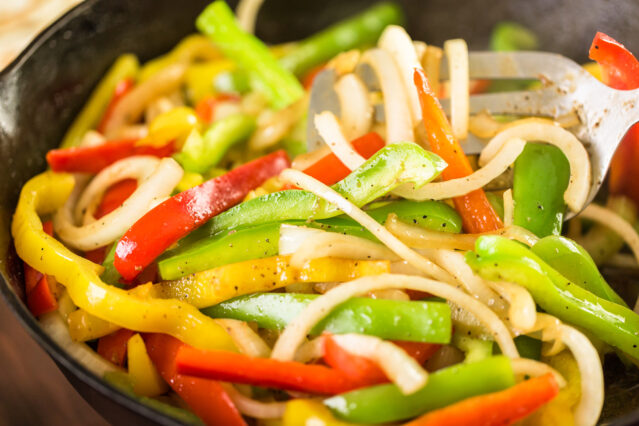 Green, yellow, and red bell peppers and onions in a cast iron pan