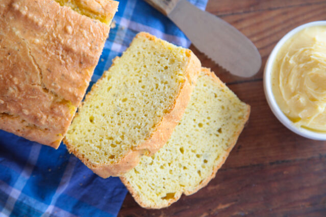 Loaf of bread sliced with ramekin of butter and a knife.