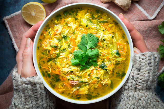 Overhead shot of a large bowl of ginger turmeric chicken soup with fresh parsley.