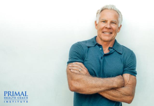 Mark stands smiling with arms crossed in front of white background with text "Primal Health Coach Institute."