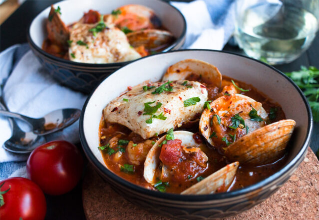 Close-up shot of two bowls of cioppino, fresh tomatoes.