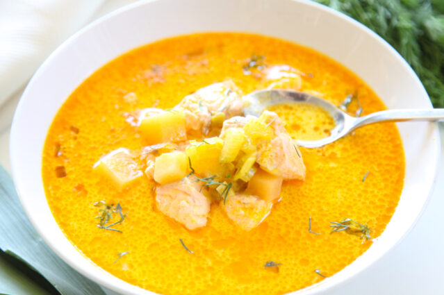 White bowl of orange-hued salmon chowder with spoon.